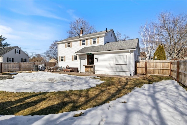 snow covered property with a patio, a chimney, and a fenced backyard