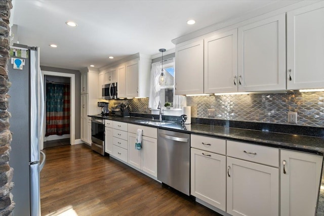 kitchen with dark wood-style floors, hanging light fixtures, white cabinets, appliances with stainless steel finishes, and backsplash