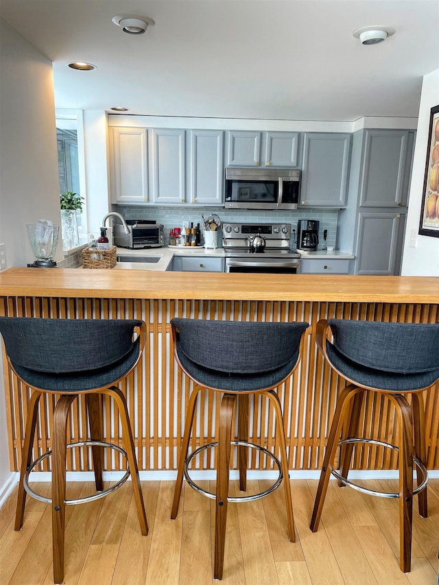 kitchen featuring light wood-type flooring, a breakfast bar, a sink, appliances with stainless steel finishes, and decorative backsplash