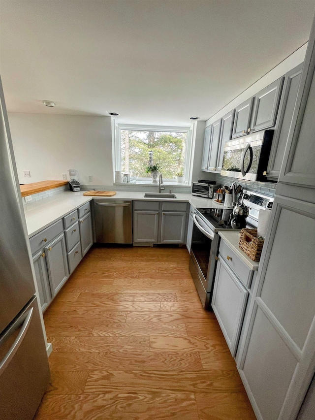 kitchen with a sink, appliances with stainless steel finishes, light wood-style flooring, and gray cabinets