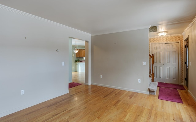 empty room featuring light wood finished floors, stairs, baseboards, and ornamental molding