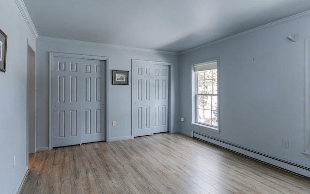 unfurnished bedroom with crown molding, light wood finished floors, multiple closets, and baseboard heating