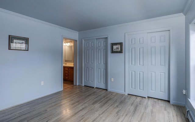 unfurnished bedroom featuring crown molding, baseboards, multiple closets, wood finished floors, and ensuite bath