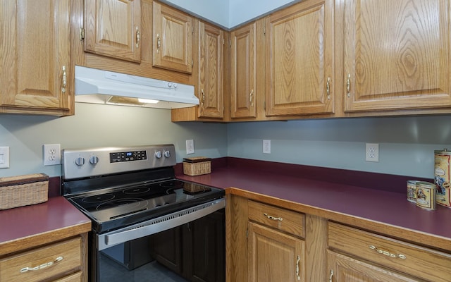 kitchen featuring under cabinet range hood, range with electric cooktop, dark countertops, and brown cabinets