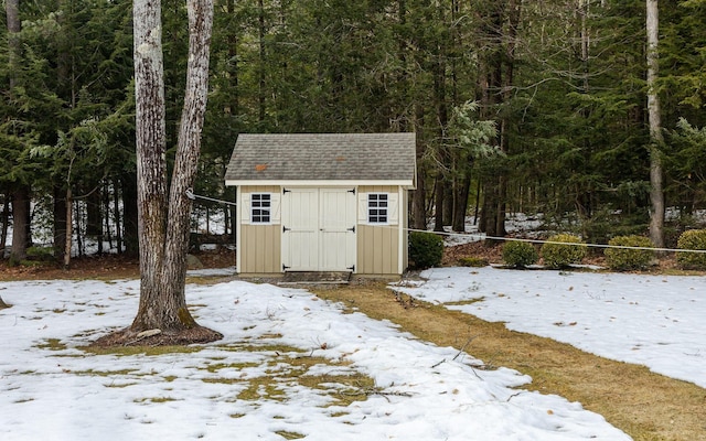 snow covered structure featuring an outdoor structure, a forest view, and a shed