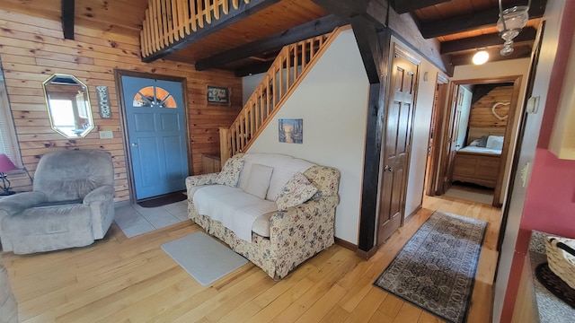 living room featuring beam ceiling, light wood-style flooring, stairway, wooden walls, and wooden ceiling