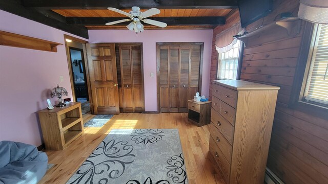 bedroom featuring light wood-style flooring, beamed ceiling, and multiple closets