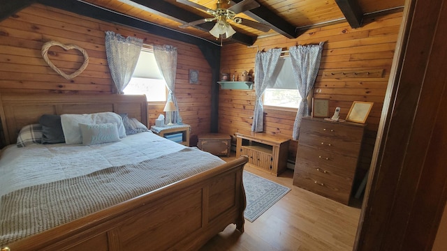 bedroom with beam ceiling, light wood-style flooring, a ceiling fan, wooden walls, and wood ceiling