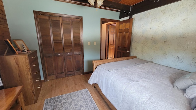 bedroom with light wood-style flooring, beamed ceiling, and a closet