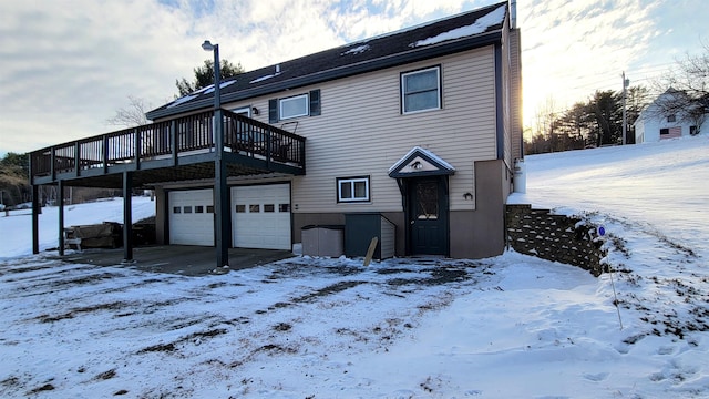 snow covered back of property featuring an attached garage and a deck