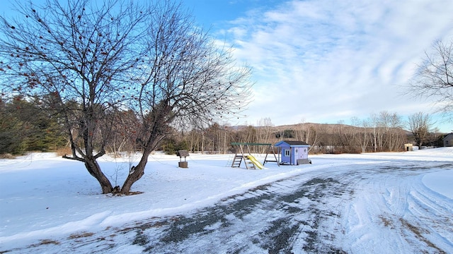 yard layered in snow featuring a wooded view and a playground