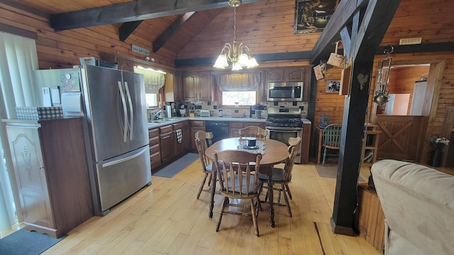 kitchen with wooden walls, vaulted ceiling with beams, light wood-style floors, appliances with stainless steel finishes, and a notable chandelier