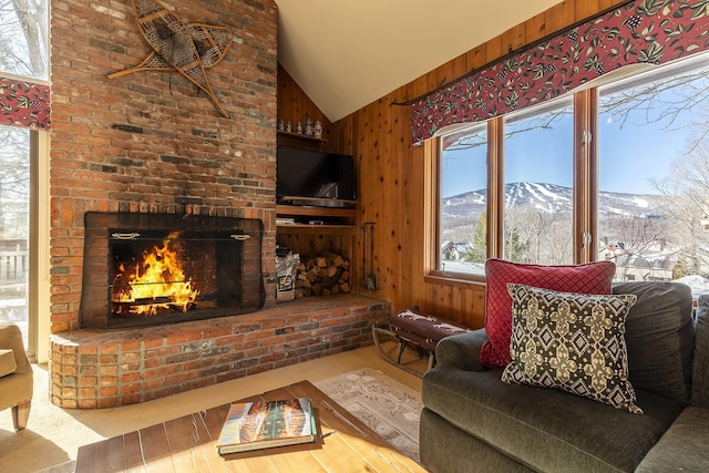 living area with a wealth of natural light, lofted ceiling, a brick fireplace, and wood walls