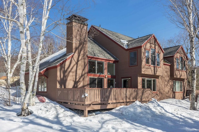 snow covered rear of property with a wooden deck and a chimney