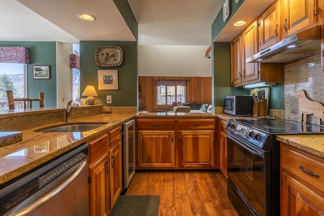 kitchen featuring under cabinet range hood, light wood-style floors, brown cabinetry, stainless steel appliances, and a sink