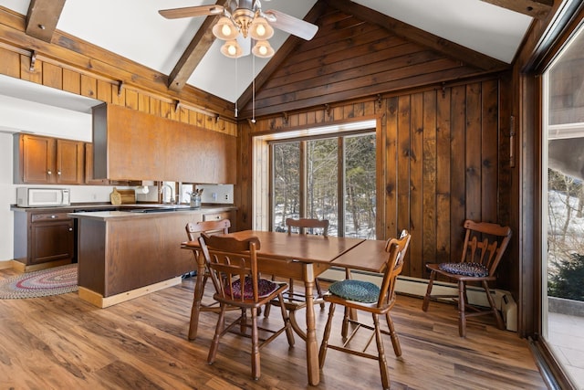 dining space with wooden walls, vaulted ceiling with beams, ceiling fan, and wood finished floors