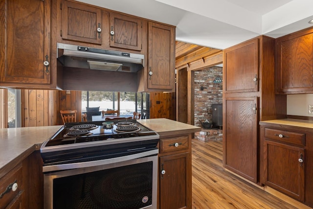 kitchen with under cabinet range hood, stainless steel electric stove, light wood-style floors, brown cabinetry, and light countertops