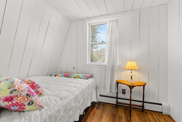 bedroom with baseboard heating, wood finished floors, and wood walls