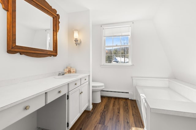 bathroom with toilet, vanity, a baseboard heating unit, and wood finished floors