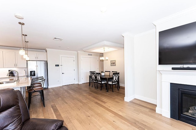 living area featuring baseboards, visible vents, ornamental molding, a glass covered fireplace, and light wood-type flooring