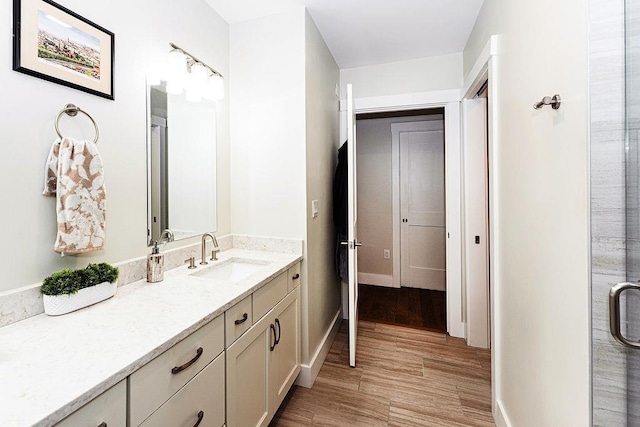 bathroom with a shower with shower door, vanity, baseboards, and wood finished floors