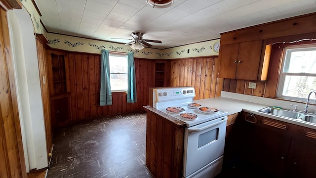 kitchen with wooden walls, light countertops, a peninsula, white electric range oven, and a sink