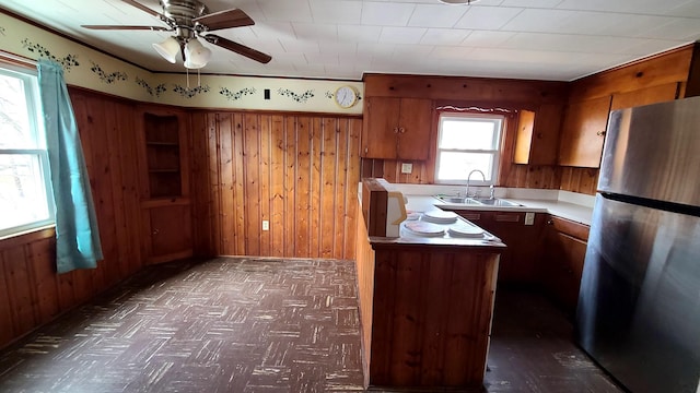 kitchen featuring a sink, wooden walls, brown cabinetry, and freestanding refrigerator