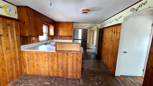 kitchen featuring light countertops, a peninsula, freestanding refrigerator, brown cabinetry, and a sink