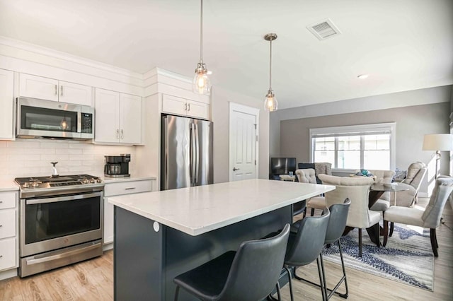 kitchen with visible vents, light countertops, appliances with stainless steel finishes, a kitchen bar, and open floor plan