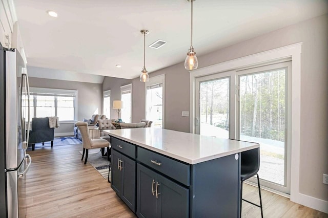 kitchen with visible vents, a breakfast bar, light wood-type flooring, light countertops, and freestanding refrigerator