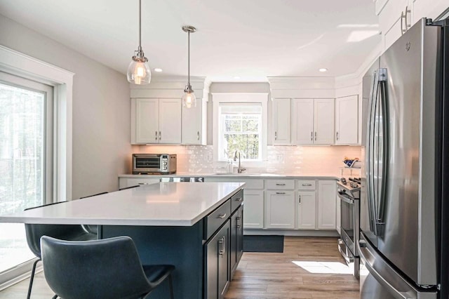 kitchen with light wood finished floors, light countertops, decorative backsplash, stainless steel appliances, and white cabinetry