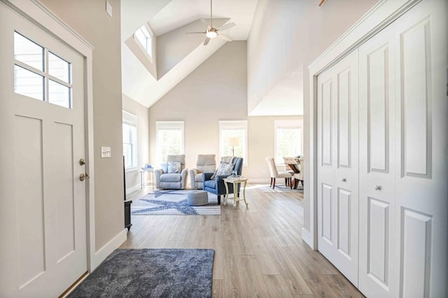 foyer featuring light wood finished floors, high vaulted ceiling, baseboards, and a ceiling fan