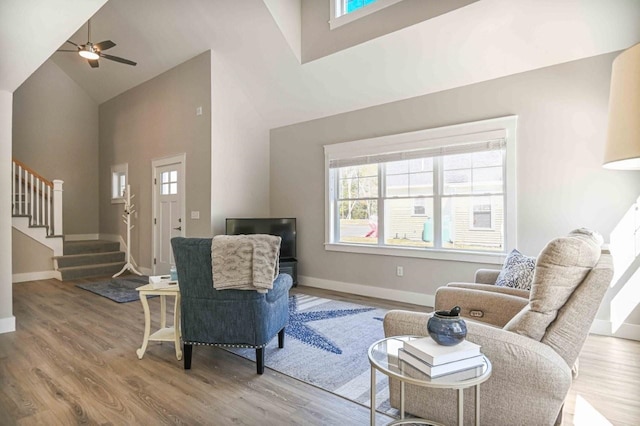 living area with stairway, high vaulted ceiling, a healthy amount of sunlight, and wood finished floors