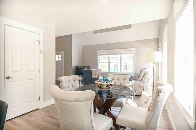 dining area featuring light wood-type flooring, baseboards, and vaulted ceiling