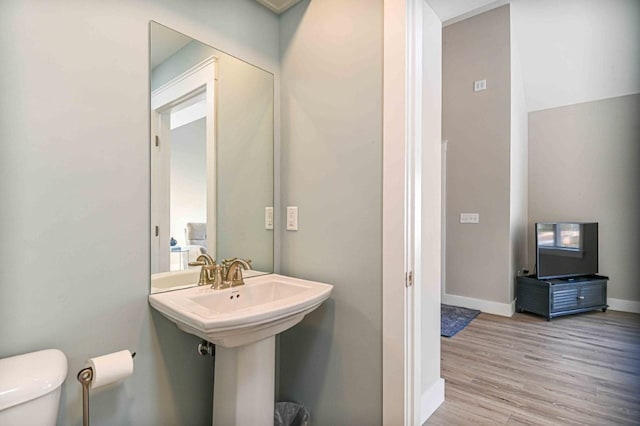 bathroom with toilet, wood finished floors, baseboards, and a sink