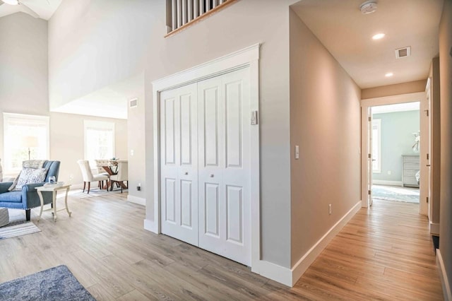 hallway featuring visible vents, baseboards, a towering ceiling, and light wood finished floors