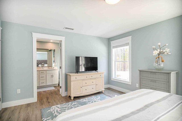 bedroom featuring visible vents, ensuite bath, baseboards, and wood finished floors