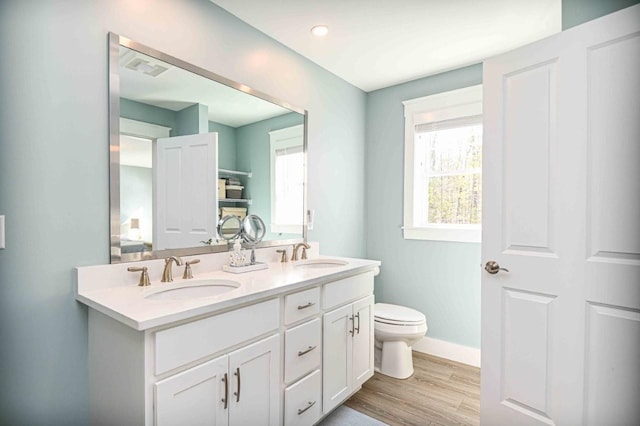 bathroom featuring double vanity, toilet, wood finished floors, and a sink