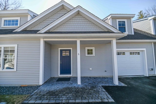 entrance to property with driveway, a porch, an attached garage, and a shingled roof