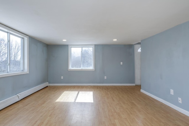 empty room featuring recessed lighting, a baseboard radiator, baseboards, and light wood-style flooring