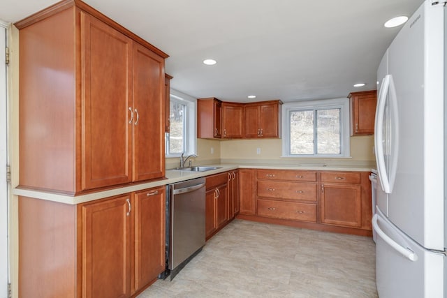 kitchen featuring brown cabinets, a sink, freestanding refrigerator, light countertops, and dishwasher