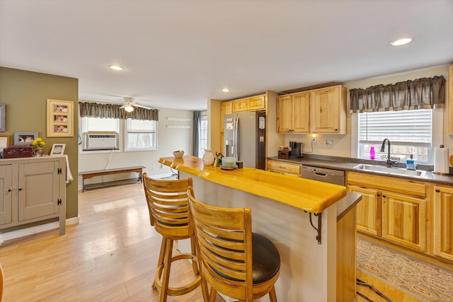 kitchen with light wood-style flooring, a sink, appliances with stainless steel finishes, a kitchen breakfast bar, and a center island