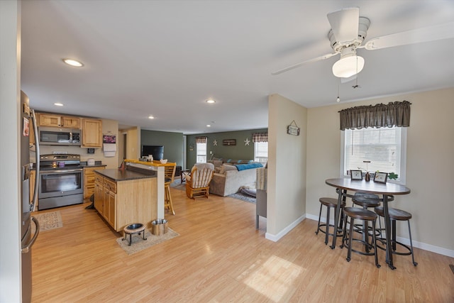 kitchen with dark countertops, baseboards, light wood-style flooring, a kitchen breakfast bar, and stainless steel appliances