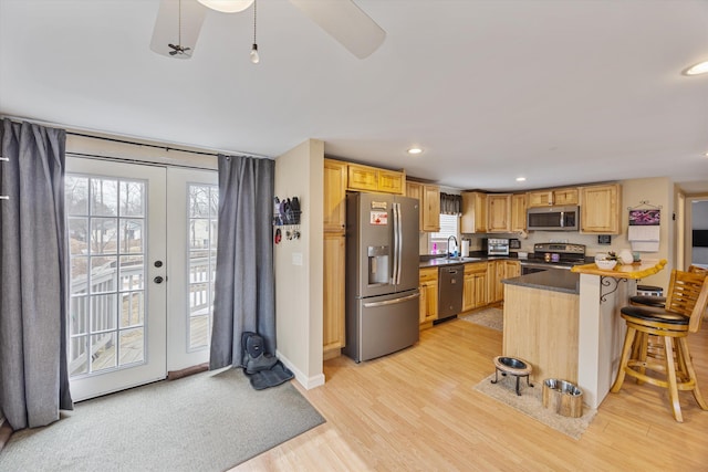 kitchen with a kitchen breakfast bar, dark countertops, french doors, appliances with stainless steel finishes, and light wood finished floors