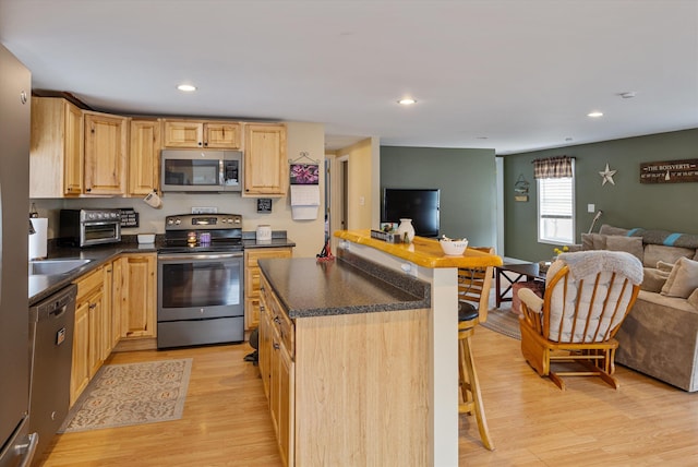 kitchen featuring dark countertops, open floor plan, light brown cabinets, and stainless steel appliances