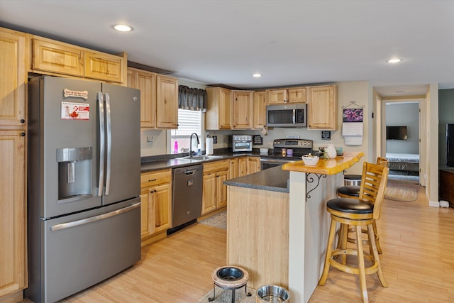 kitchen with a sink, light wood-type flooring, a kitchen breakfast bar, and appliances with stainless steel finishes