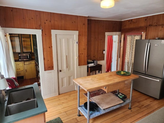 kitchen featuring wood walls, appliances with stainless steel finishes, light wood-style floors, and a sink