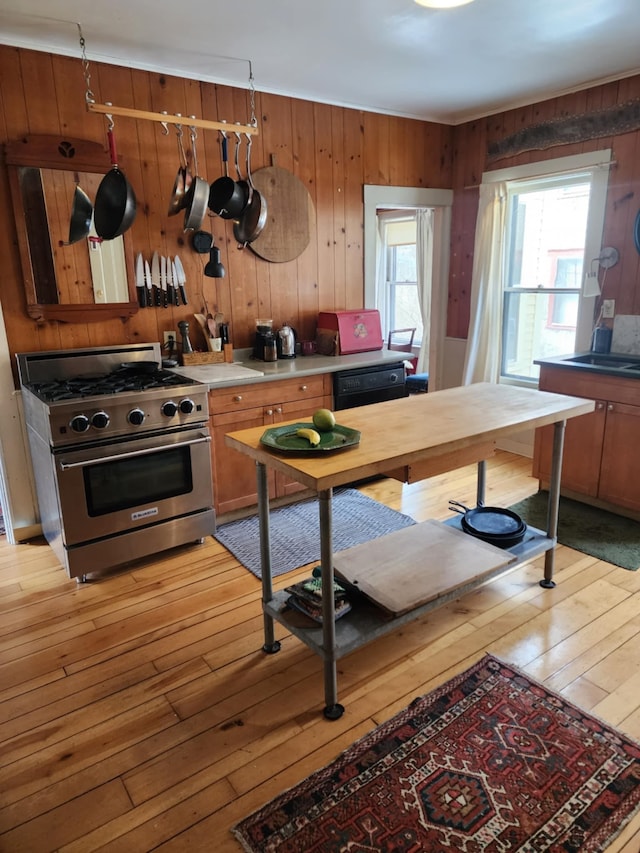 kitchen featuring light wood-type flooring, stainless steel stove, wood walls, and light countertops