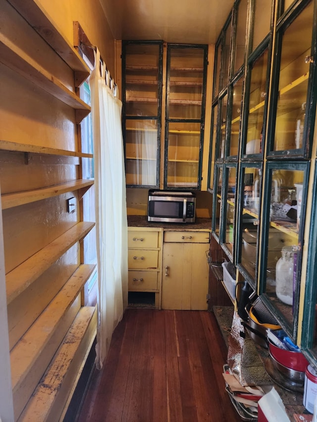 kitchen with dark wood-style floors, stainless steel microwave, dark countertops, and open shelves