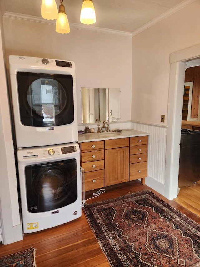 laundry room featuring a wainscoted wall, ornamental molding, a sink, stacked washing maching and dryer, and laundry area